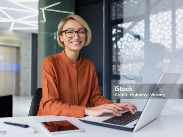 Portrait of happy and successful female programmer inside office at workplace, worker smiling and looking at camera with laptop blonde businesswoman is satisfied with results of achievements at work